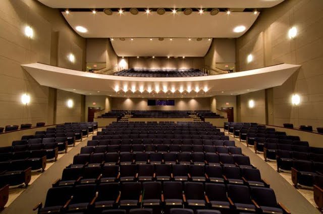 unnamed Empty auditorium with rows of dark seats, balcony level, and stage lighting, viewed from the stage facing the audience area.